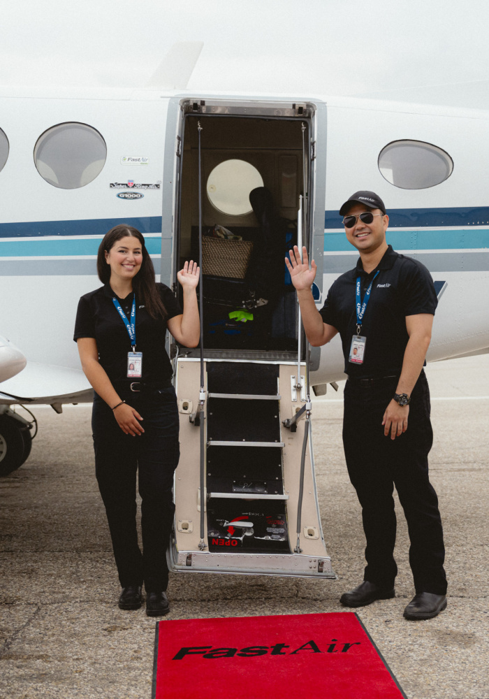 Two pilots waving while standing outside a King Air aircraft on the tarmac.